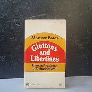 May include: A vintage paperback book titled "Gluttons and Libertines: Human Problems of Being Natural" by Marston Bates. The cover features a yellow and red illustration of a half-circle with the title in white text.