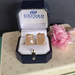 May include: A pair of gold-toned rectangular earrings with a light brown stone in a blue velvet jewelry box with the text "Oxford Diamond" on the lid.