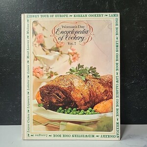 Puede incluir: Un libro de cocina vintage titulado "Woman's Day Encyclopedia of Cookery", volumen 7, con una foto de un plato de carne asada en un plato blanco con guisantes verdes y zanahorias.