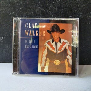May include: A music CD case featuring the album cover for Clay Walker's If I Could Make a Living. The cover displays a photograph of a person wearing a black cowboy hat and a black shirt with orange and white arrow patterns, set against a blue background.