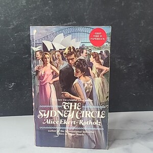 以下が含まれることがあります： アリス・エカート＝ロトホルツ著の「シドニー・サークル」というタイトルのペーパーバック。表紙には、カップルと群衆のヴィンテージイラストが描かれており、背景にはシドニーオペラハウスが描かれています。「First Time in Paperback!」というテキストも含まれています。