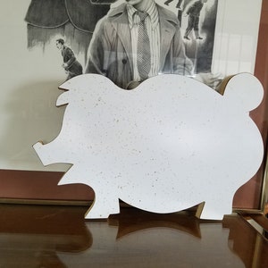 May include: White ceramic piggy bank shaped like a pig with a speckled texture. The piggy bank is sitting on a wooden surface.