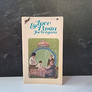 Puede incluir: Un libro de bolsillo vintage titulado "Love & Pasta" de Joe Vergara. La portada presenta una ilustración de una familia reunida alrededor de una mesa a cuadros. El libro tiene una cubierta color crema con texto turquesa y verde.