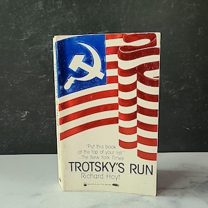 May include: A paperback book titled "Trotsky's Run" by Richard Hoyt. The cover features a stylized design with a blue section containing a hammer and sickle, and red and white stripes. The book has a quote from The New York Times.