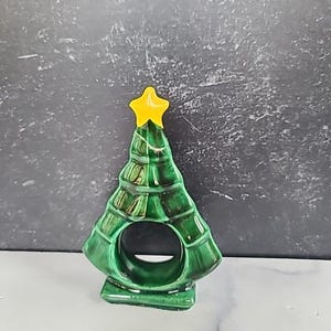 Puede incluir: Un anillo de servilleta de cerámica verde en forma de árbol de Navidad con una estrella amarilla en la parte superior.