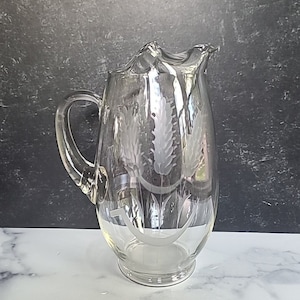 May include: A clear glass pitcher with an etched wheat design. The pitcher has a wide mouth and a handle.