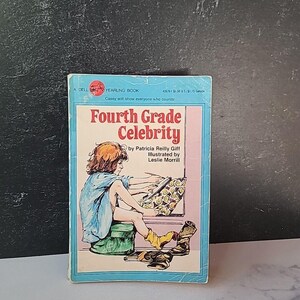 May include: A blue and pink book cover with the title "Fourth Grade Celebrity" by Patricia Reilly Giff. The cover features an illustration of a young girl sitting on a green stool, drawing on a pad of paper.