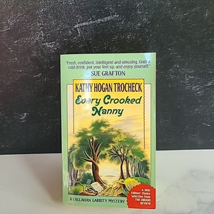 May include: A paperback book titled "Every Crooked Nanny" by Kathy Hogan Trocheck. It is a Callahan Garrity mystery and a 1992 Editors' Choice Selection from The Drood Review. The cover features a colorful illustration of a forest scene with two trees and a path leading to a clearing.