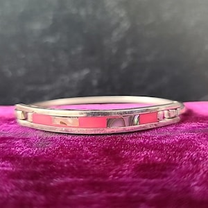 Peut inclure: Un bracelet en argent avec une incrustation rose et blanche. Le bracelet est sur une surface en velours rose.