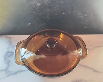 May include: A brown glass casserole dish with a lid. The dish has two handles on the sides.