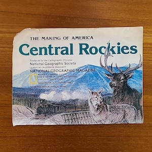 May include: A vintage National Geographic Magazine cover titled "Central Rockies." The cover features illustrations of a deer, a wolf, a train, and a mountain landscape. Text includes "The Making of America" and "August 1984."