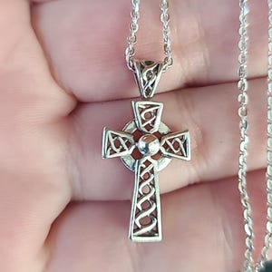 May include: A silver Celtic cross pendant necklace. The cross features intricate openwork designs and a central orb. The pendant hangs from a delicate silver chain, creating a classic and elegant look.