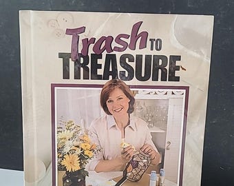 以下が含まれることがあります： 「Trash to Treasure: The Year's Best Creative Crafts」というタイトルの本。表紙には、ステンドグラスのプロジェクトに取り組んでいる女性が写っています。