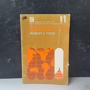 May include: A vintage book titled "Comparative Political Institutions" by Robert C. Fried. The cover is a golden-brown color with orange and white graphics, including a world map and a building illustration. The book is part of the "Government in the Modern World" series.