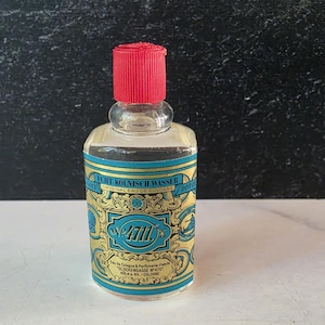 May include: A clear glass bottle of 4711 Original Eau de Cologne with a bright red cap. The label features a blue and gold ornate design with the text ECHT KÖLNISCH WASSER, 4711, and Eau de Cologne & Parfümerie-Fabrik Glockengasse No 4711.
