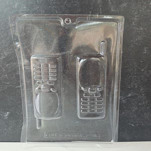 May include: Clear plastic mold with two retro cell phone designs. One mold features a phone with a keypad and the other has a keypad and antenna. The text "LIFE OF THE PARTY" is visible at the bottom of the mold.