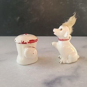 May include: White ceramic salt and pepper shakers shaped like a fire hydrant and a dog. The dog has a red collar and a fluffy white tail.