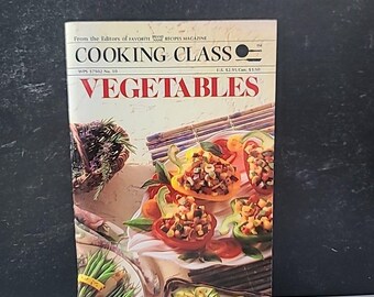 Puede incluir: Un libro de cocina titulado "COOKING CLASS VEGETABLES" con una portada que presenta pimientos rellenos. La portada también muestra texto de "FAVORITE RECIPES MAGAZINE". El libro está sobre un fondo oscuro.