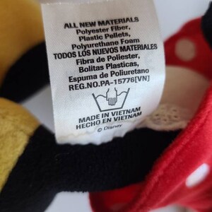 K&ouml;nnte beinhalten: Ein Etikett von einem Disney-Pl&uuml;schtier mit Text in Englisch und Spanisch. Das Etikett listet Materialien wie Polyesterfaser und Polyurethanschaum auf. Das Etikett gibt auch an, dass das Spielzeug in Vietnam hergestellt wurde.