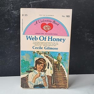 Puede incluir: Una portada de libro de bolsillo con un diseño rosa y blanco. El título es "Web Of Honey" de Cecile Gilmore. La portada presenta a una mujer con una camisa azul y un hombre con traje.