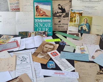 May include: A collection of vintage postcards, letters, and ephemera, including a Walgreens Suncare Guide, a postcard with a woman in a swimsuit, a postcard with a man in a swimsuit, a postcard with a waterfall, a postcard with a religious image, and a postcard with a quote about justice. The items are arranged on a gray surface.