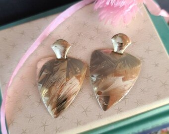 May include: A pair of silver earrings with a triangular shape and a textured surface. The earrings have a brushed metal finish and a slightly iridescent sheen.