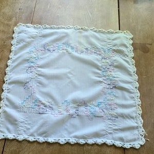 May include: White crocheted square tablecloth with a colorful embroidered border.