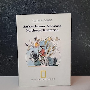 May include: A National Geographic book titled "CLOSE-UP: CANADA" featuring the provinces of Saskatchewan, Manitoba, and Northwest Territories. The cover illustration depicts a person on horseback, surrounded by wheat and birds.