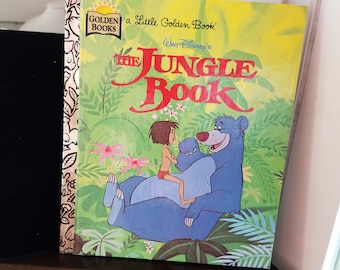 May include: A Little Golden Book with a yellow cover featuring a cartoon image of Baloo the bear from Disney's The Jungle Book. Baloo is holding Mowgli, the boy who was raised by wolves, in his arms. The book's title is "The Jungle Book" with the words "Walt Disney's" in parentheses below the title.