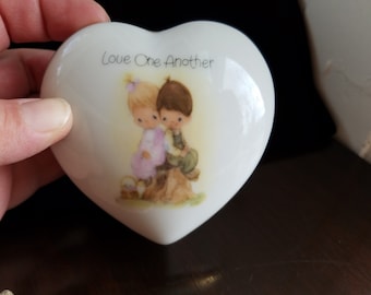 Puede incluir: Caja de cerámica blanca en forma de corazón con una imagen pintada de dos niños tomados de la mano y el texto "Love One Another".