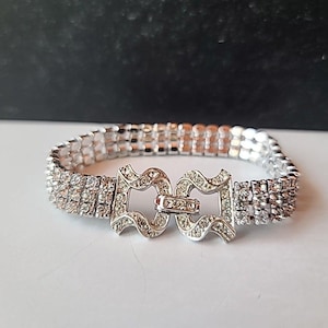 May include: Silver-toned bracelet with a decorative clasp. The bracelet is adorned with multiple rows of small, sparkling rhinestones. The clasp features an ornate design with additional rhinestones, adding to the bracelet's overall elegance and sparkle.
