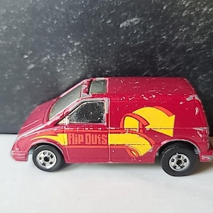 May include: A vintage red toy van with yellow and red graphics, and the text "Flip Outs" on the side. The toy van has black wheels and a small sunroof. The van is a collectible item.