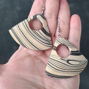 Puede incluir: Un par de pendientes geométricos con un diseño de mármol blanco y negro. Los pendientes tienen forma de abanico con un recorte circular en el centro.