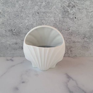 May include: White ceramic seashell shaped candle holder. The holder is designed to look like a seashell with a smooth, white finish.