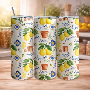 May include: Three stainless steel tumblers with lids and straws. The tumblers feature a repeating pattern of lemons, green leaves, terracotta pots, and blue and yellow geometric tiles. Text includes "Dolce Vita", "Amore", "Estate", and "Limoni".