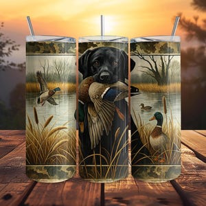Può includere: Tre bicchieri isolati in acciaio inossidabile a tema caccia. Ogni bicchiere presenta un Labrador Retriever nero che tiene delle anatre in bocca, con uno sfondo di un lago e delle anatre. I bicchieri hanno un motivo mimetico nella parte superiore e inferiore.