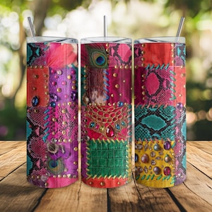 Op de afbeelding: Drie roestvrijstalen bekers met deksels en rietjes. Elke beker heeft een patchwork-ontwerp met imitatieleer, slangenprint en juweelversieringen in roze, paarse, oranje en blauwgroene tinten. Het ontwerp bevat pauwenveren en gouden studs.
