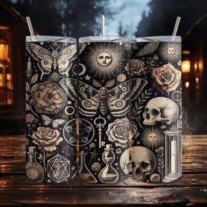 Puede incluir: Tres vasos de acero inoxidable negros con intrincadas ilustraciones blancas de polillas, mariposas, rosas, calaveras y elementos celestiales. Cada vaso tiene una tapa plateada y una pajita transparente. El diseño tiene un tema gótico y oculto.