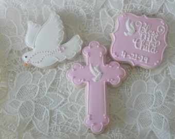 Op de afbeelding: Drie gedecoreerde suikerkoekjes. Een koekje is gevormd als een duif, een ander als een kruis en de derde is een rechthoekig koekje met de tekst "Bless This Child" en de datum "4-21-19".
