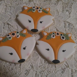 May include: Three fox-shaped sugar cookies decorated with orange icing, white frosting, and floral accents. The cookies have black eyes and a black nose.