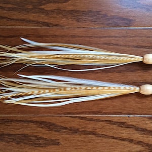 May include: A pair of feather earrings with a wooden bead and gold hook. The feathers are white and brown with a light brown stripe down the center.