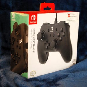 May include: A black Nintendo Switch wired controller in its original white and red packaging. The box features the Nintendo Switch logo, the text Wired Controller, and a clear image of the controller with dual analog sticks and buttons.