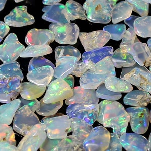Könnte beinhalten: Eine Sammlung von irisierenden Opal-Chips in verschiedenen Blautönen, Grüntönen und Weißtönen. Die Chips sind unregelmäßig geformt und haben eine natürliche, raue Textur.