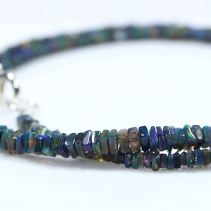 May include: A black opal gemstone necklace with a silver clasp. The necklace is made of small, rectangular-shaped beads.