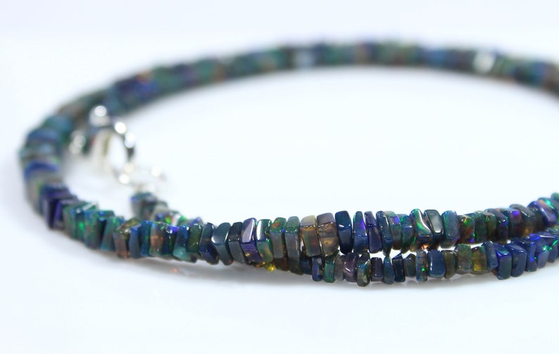 May include: A black opal gemstone necklace with a silver clasp. The necklace is made of small, rectangular-shaped beads.