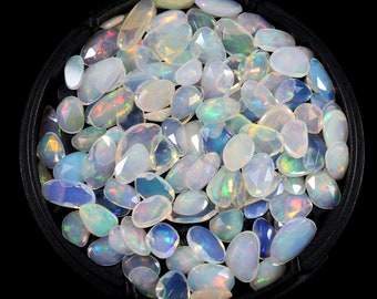 Pode incluir: Uma coleção de gemas de opala branca em vários formatos e tamanhos, exibidas em uma bandeja preta. As opalas têm um brilho iridescente e são perfeitas para a fabricação de joias.