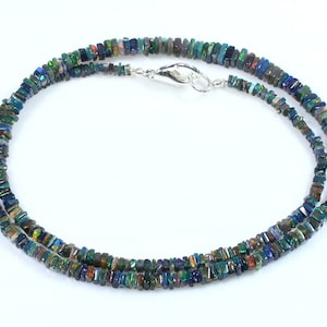 May include: A double-strand necklace made of iridescent black opal beads. The beads are rectangular in shape and have a variety of colors, including green, blue, and purple. The necklace is secured with a silver clasp.