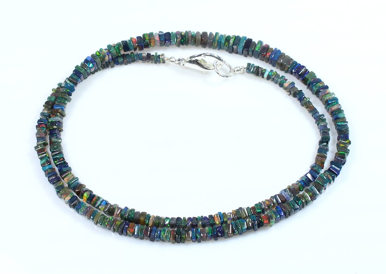 May include: A double-strand necklace made of iridescent black opal beads. The beads are rectangular in shape and have a variety of colors, including green, blue, and purple. The necklace is secured with a silver clasp.