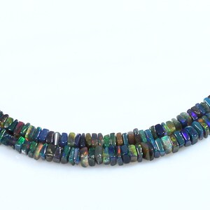 May include: A strand of black opal beads, with iridescent green, blue, and purple hues. The beads are rectangular in shape and are strung on a clear thread.