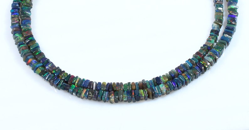 May include: A strand of black opal beads, with iridescent green, blue, and purple hues. The beads are rectangular in shape and are strung on a clear thread.